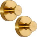 Two round brushed gold Fenas suction cup hooks mounted on a white tiled shower wall, holding a towel and a loofah.