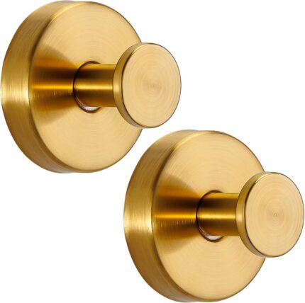 Two round brushed gold Fenas suction cup hooks mounted on a white tiled shower wall, holding a towel and a loofah.