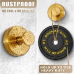 Two round brushed gold Fenas suction cup hooks mounted on a white tiled shower wall, holding a towel and a loofah.
