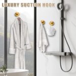 Two round brushed gold Fenas suction cup hooks mounted on a white tiled shower wall, holding a towel and a loofah.