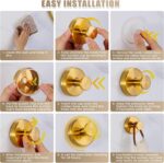 Two round brushed gold Fenas suction cup hooks mounted on a white tiled shower wall, holding a towel and a loofah.