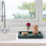 A rectangular green marble vanity tray by Sumlus, holding a small perfume bottle and a few pieces of jewelry.