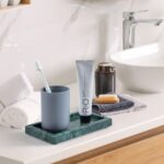 A rectangular green marble vanity tray by Sumlus, holding a small perfume bottle and a few pieces of jewelry.
