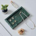 A rectangular green marble vanity tray by Sumlus, holding a small perfume bottle and a few pieces of jewelry.