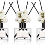 Three transparent glass bottles of WEALD TRIBE flower reed diffusers with black fiber sticks and dried flowers in a luxurious