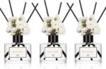 Three transparent glass bottles of WEALD TRIBE flower reed diffusers with black fiber sticks and dried flowers in a luxurious
