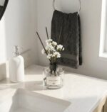 Three transparent glass bottles of WEALD TRIBE flower reed diffusers with black fiber sticks and dried flowers in a luxurious