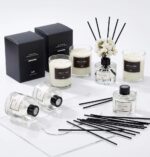 Three transparent glass bottles of WEALD TRIBE flower reed diffusers with black fiber sticks and dried flowers in a luxurious