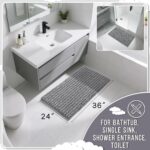 A soft, rectangular grey chenille bath mat with a shaggy texture, placed on a clean bathroom floor.