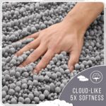 A soft, rectangular grey chenille bath mat with a shaggy texture, placed on a clean bathroom floor.