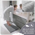 A soft, rectangular grey chenille bath mat with a shaggy texture, placed on a clean bathroom floor.